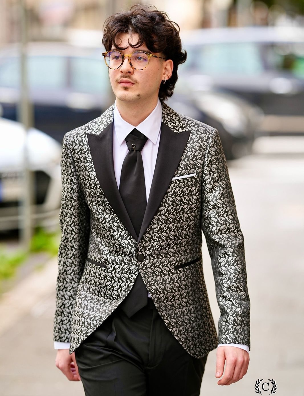 Giovane con occhiali in giacca jacquard nera e argento con revers in raso, cravatta nera, marchio Cortese Multibrand